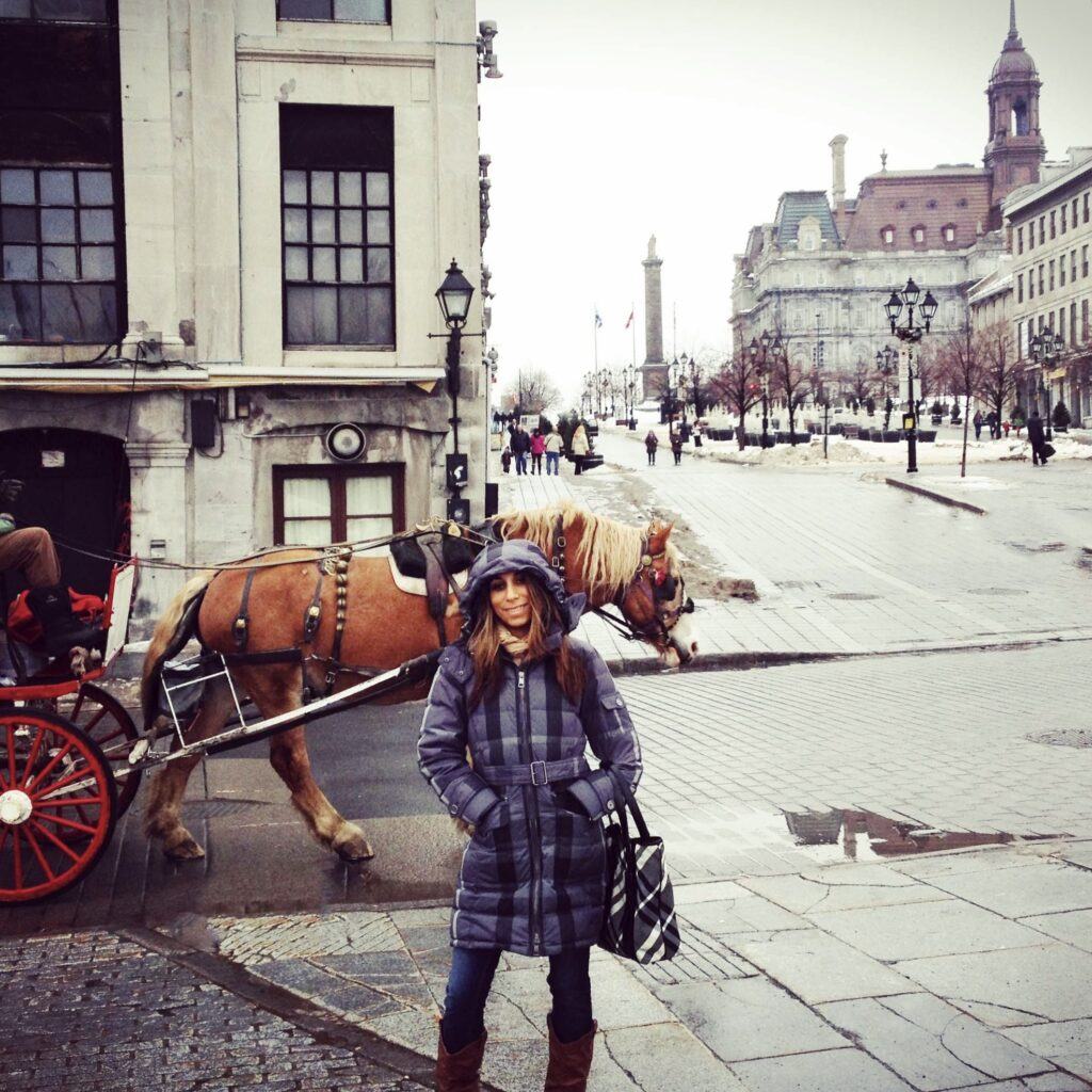 a woman standing in front of a horse pulled wagon on a street in Montreal during the wintertime