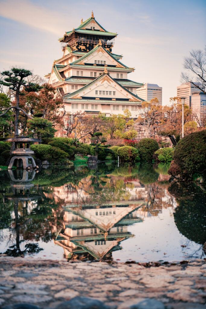 iconic Osaka Castle in Japan and its reflection in the moat framed by a vibrant autumn foliage 