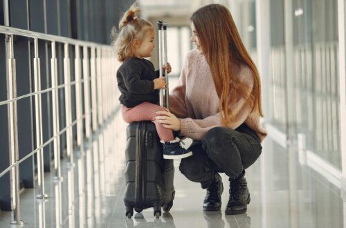 Mom talking to her toddler sitting on carry-on luggage at the airport