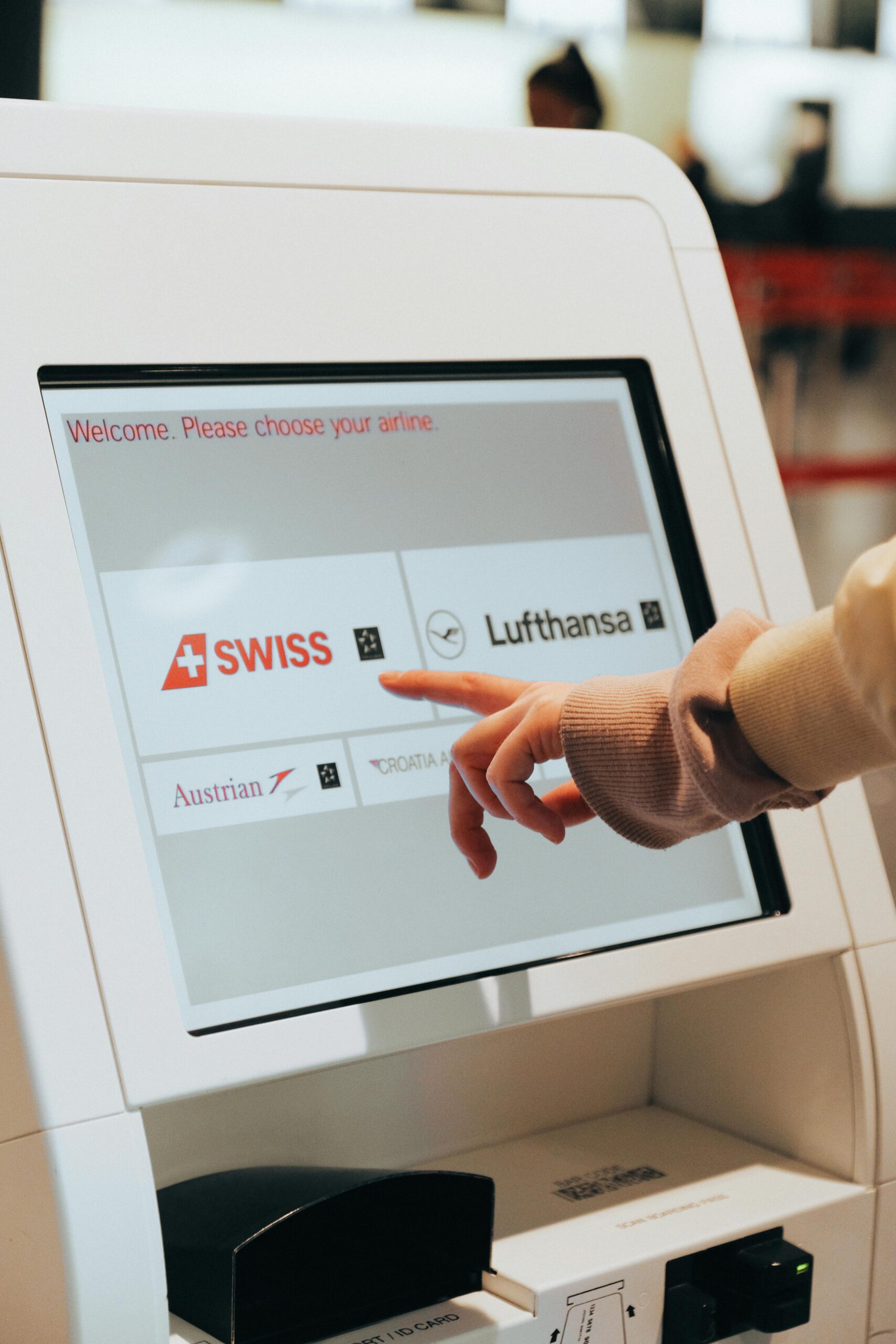 Person selecting an airline on a self-service check-in kiosk at the airport